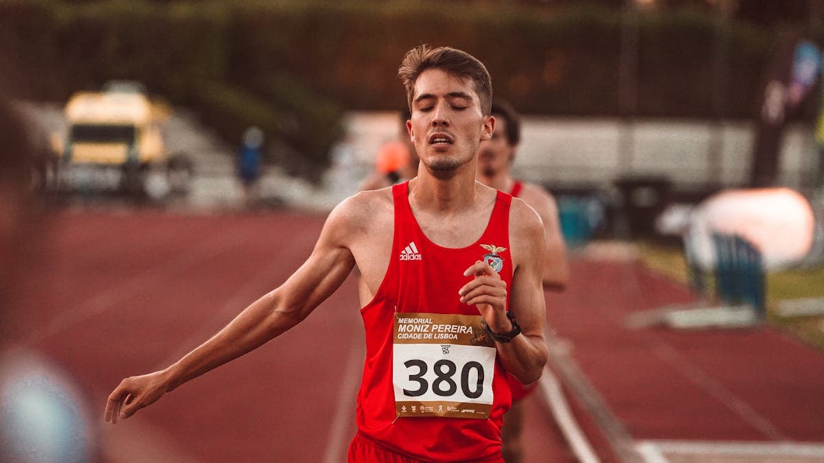 A young male runner crossing the finish line on a track, demonstrating determination and effort.